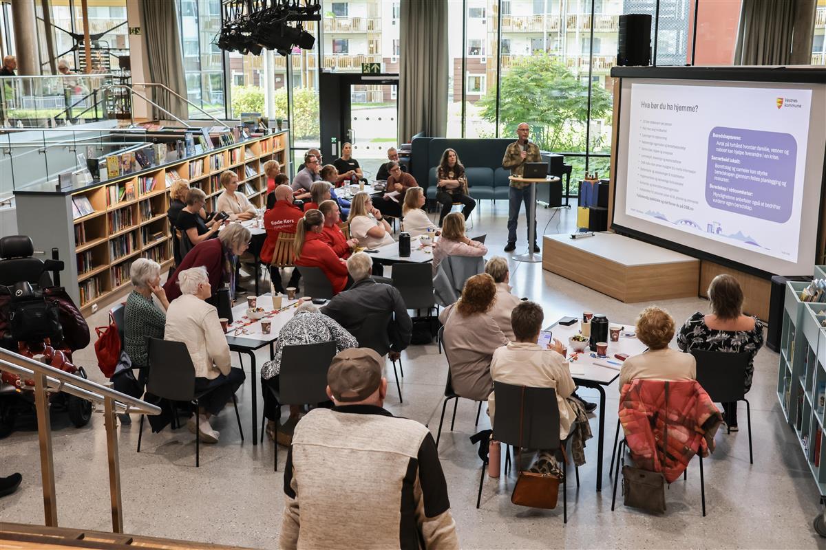 Deltakarar sit rundt bord på Vestnes bibliotek medan ein presentasjon om beredskap blir vist på storskjerm. - Klikk for stort bilete