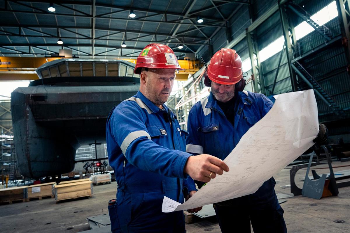 Arbeidere på et skipsverft ser på tegninger - Klikk for stort bilete