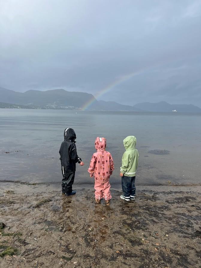 Barn i regnklede på ei strand. Regnboge i bakgrunnen - Klikk for stort bilete